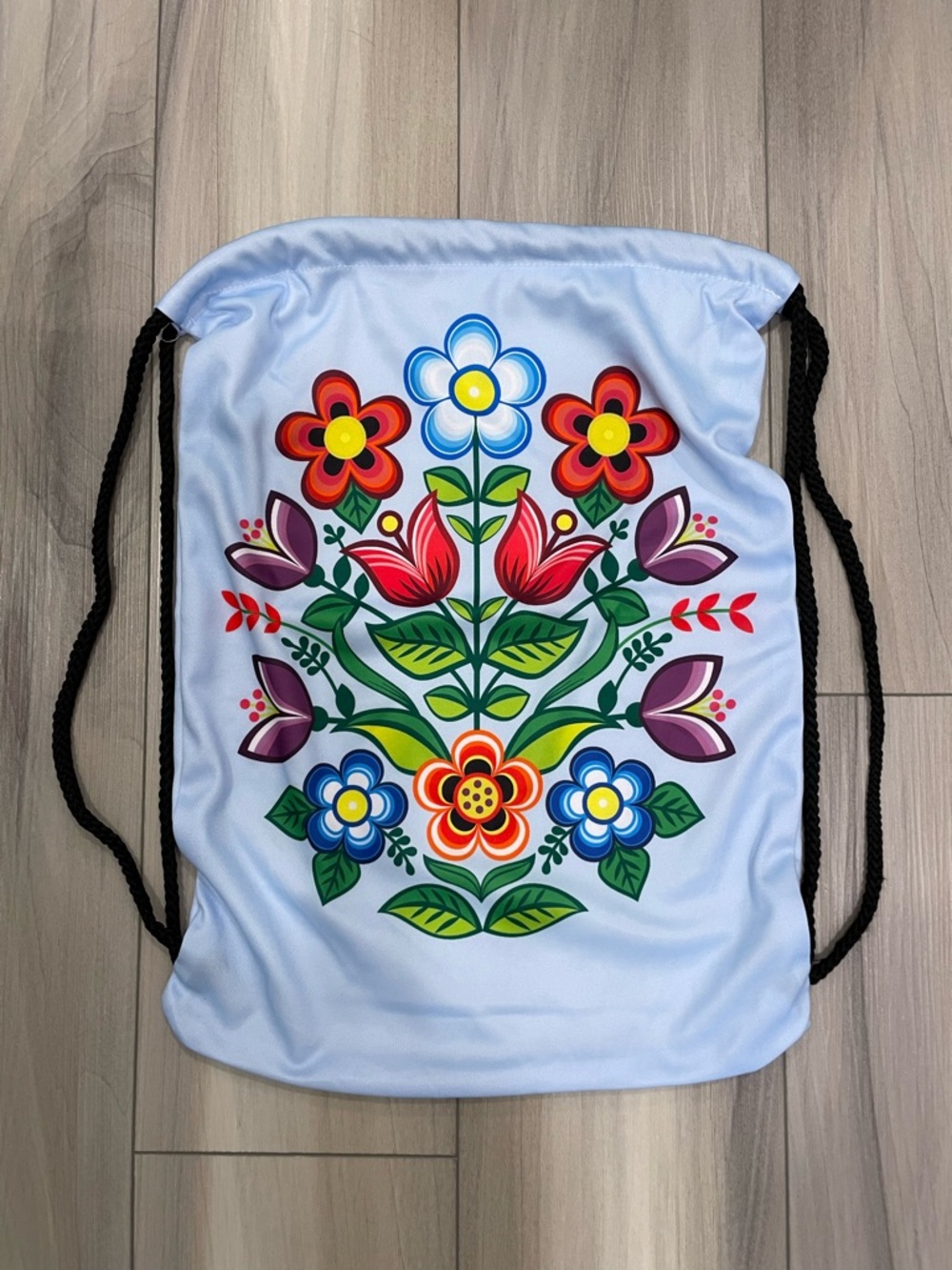 Light Blue Drawstring Bag with Vibrant Floral Design and Black Cord Drawstrings